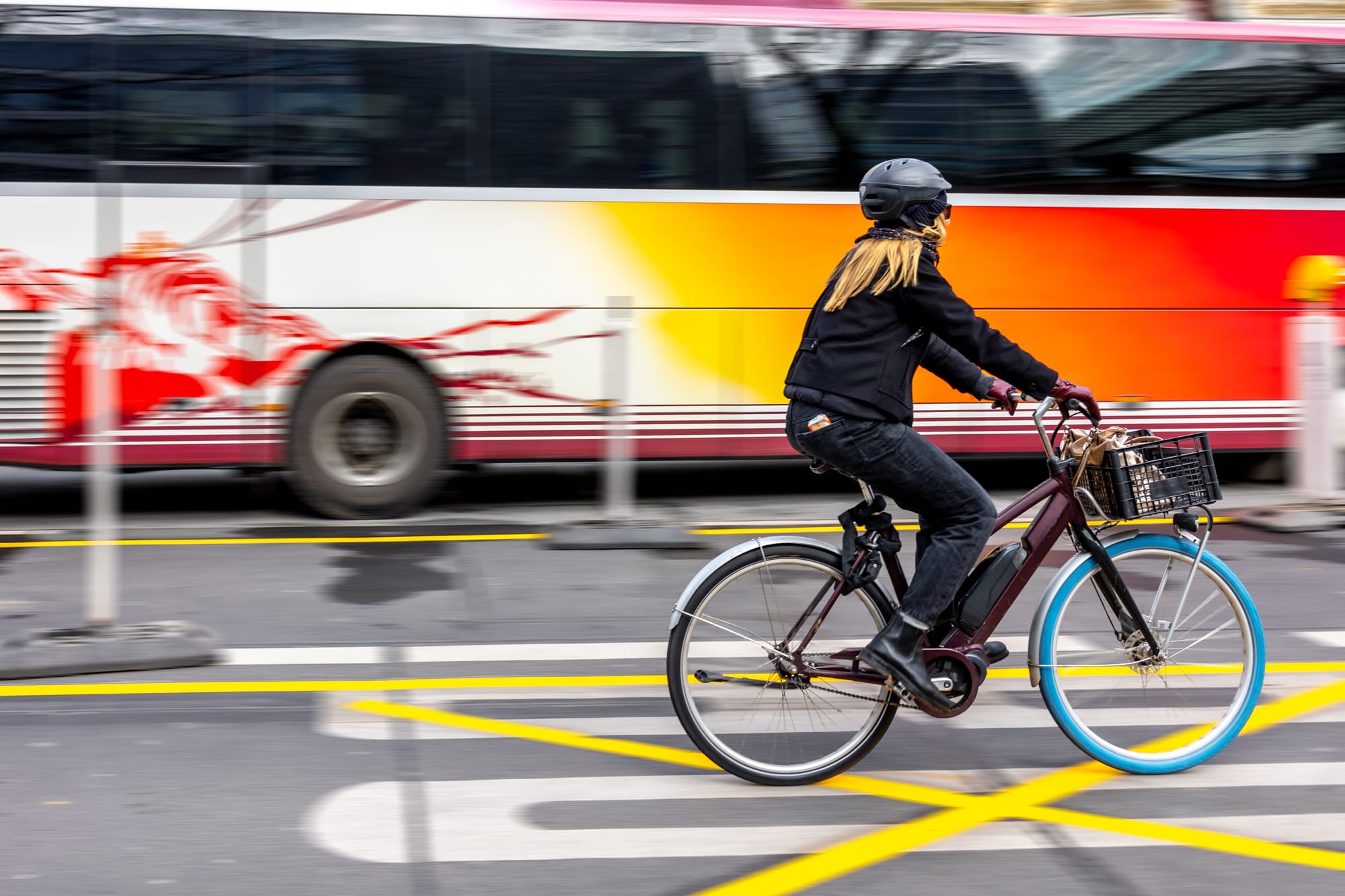 Woman riding an electric bike on a city street next to a bus.