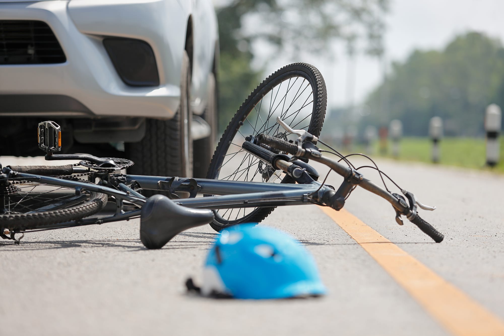 A bike on the side of the road in front of a car that has crashed into it. A blue helmet lies in front of the bike and car on the street.