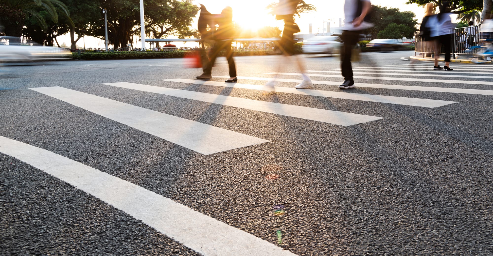 A blurred image of a group of people walking in a crosswalk with sun shining.