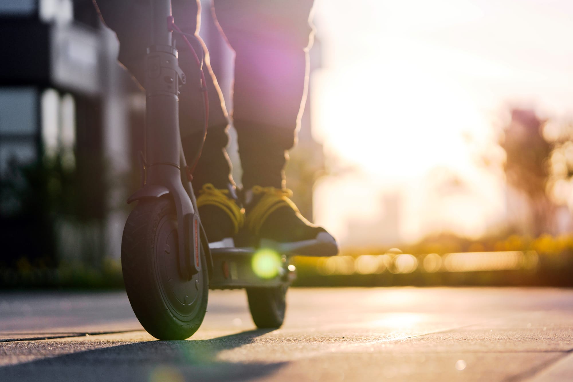 A view of a person's feet on an e-scooter in the city with the sun in the background.