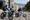 Three teens wearing helmets riding across a street in San Francisco with a trolley car and the golden gate bridge in the background.