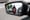 The side mirror of a car in traffic reflects a motorcyclist who is between cars.